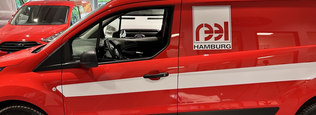 Fahrzeugbeschriftung FES Hamburg: roter Transporter mit weißem Seitenstreifen und quadratischem Logo – umgesetzt von Folien Fischer Hamburg